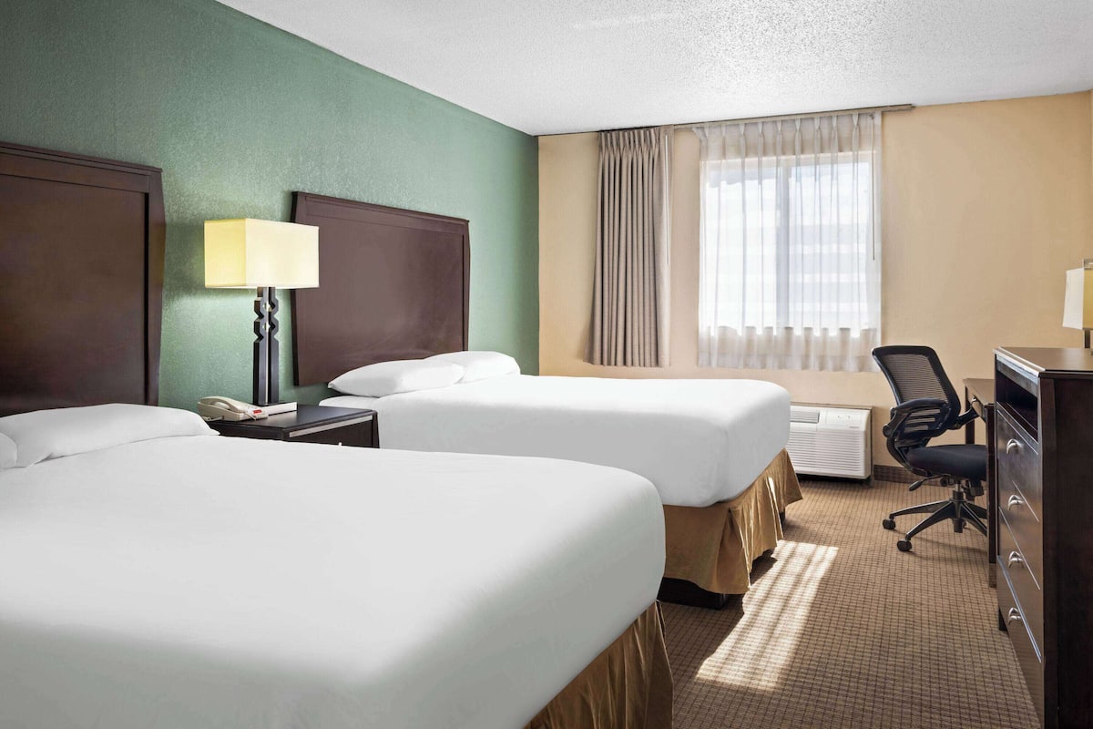 A hotel room with two beds, a desk, a chair, a lamp, and a window with curtains.