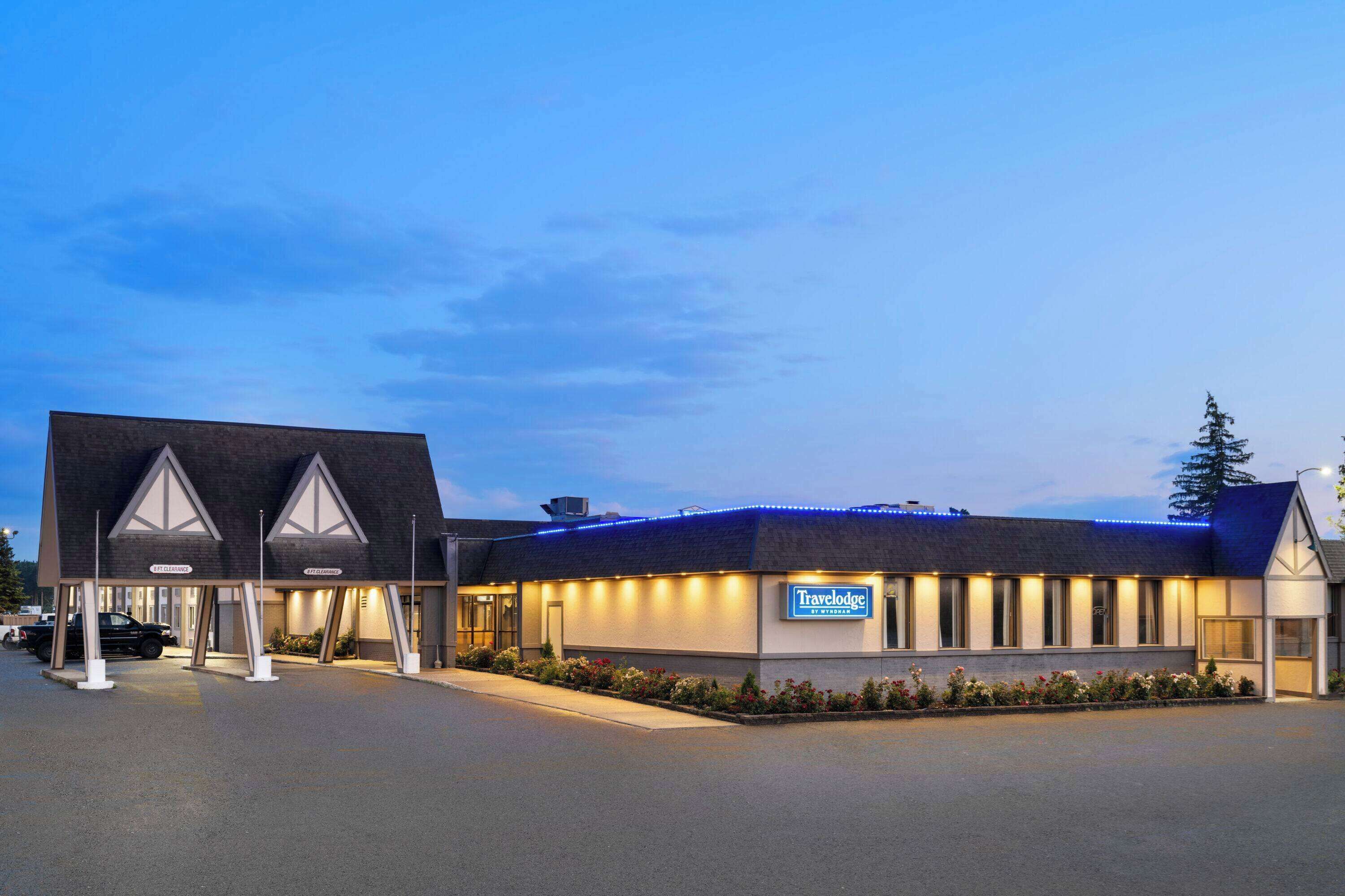 Hotel Travelodge com design moderno, apresentando uma placa grande, área de estacionamento coberta e fachada bem iluminada.