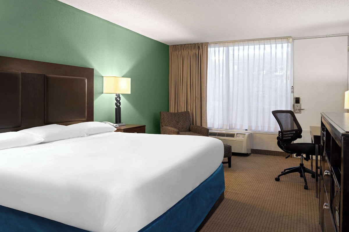 A hotel room with a large bed, a desk with a chair, a lamp, and a window with curtains.