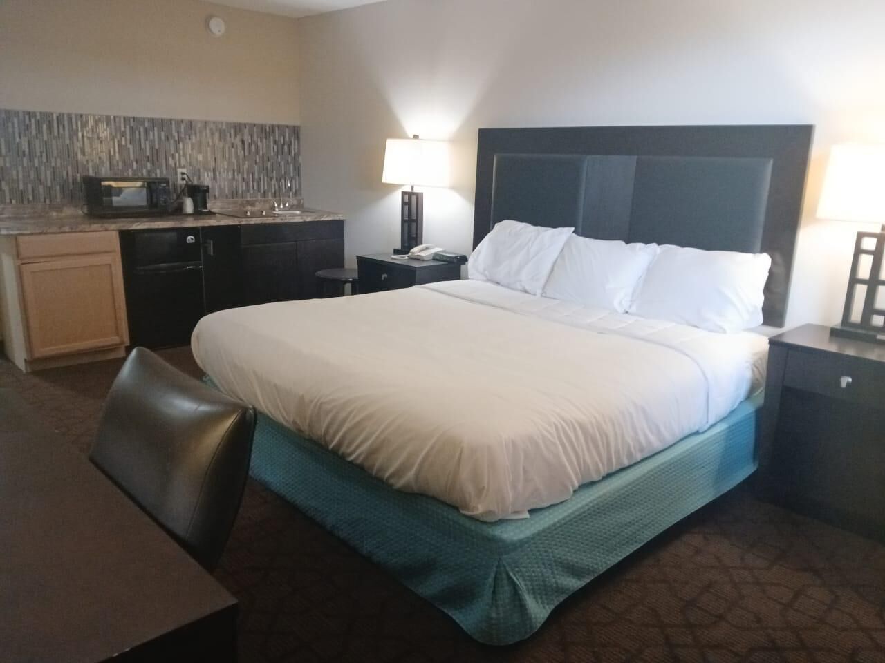 Quarto de hotel com cama, escrivaninha, micro-ondas, luminária e mesa de cabeceira.