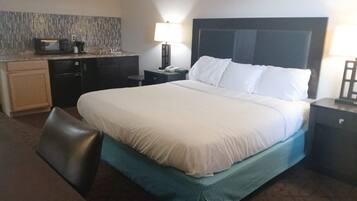 Quarto de hotel com cama, escrivaninha, micro-ondas, luminária e mesa de cabeceira.