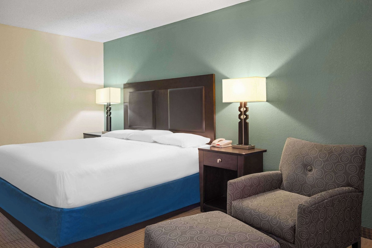 A hotel room with a large bed, two bedside tables with lamps, a chair, and a small table.