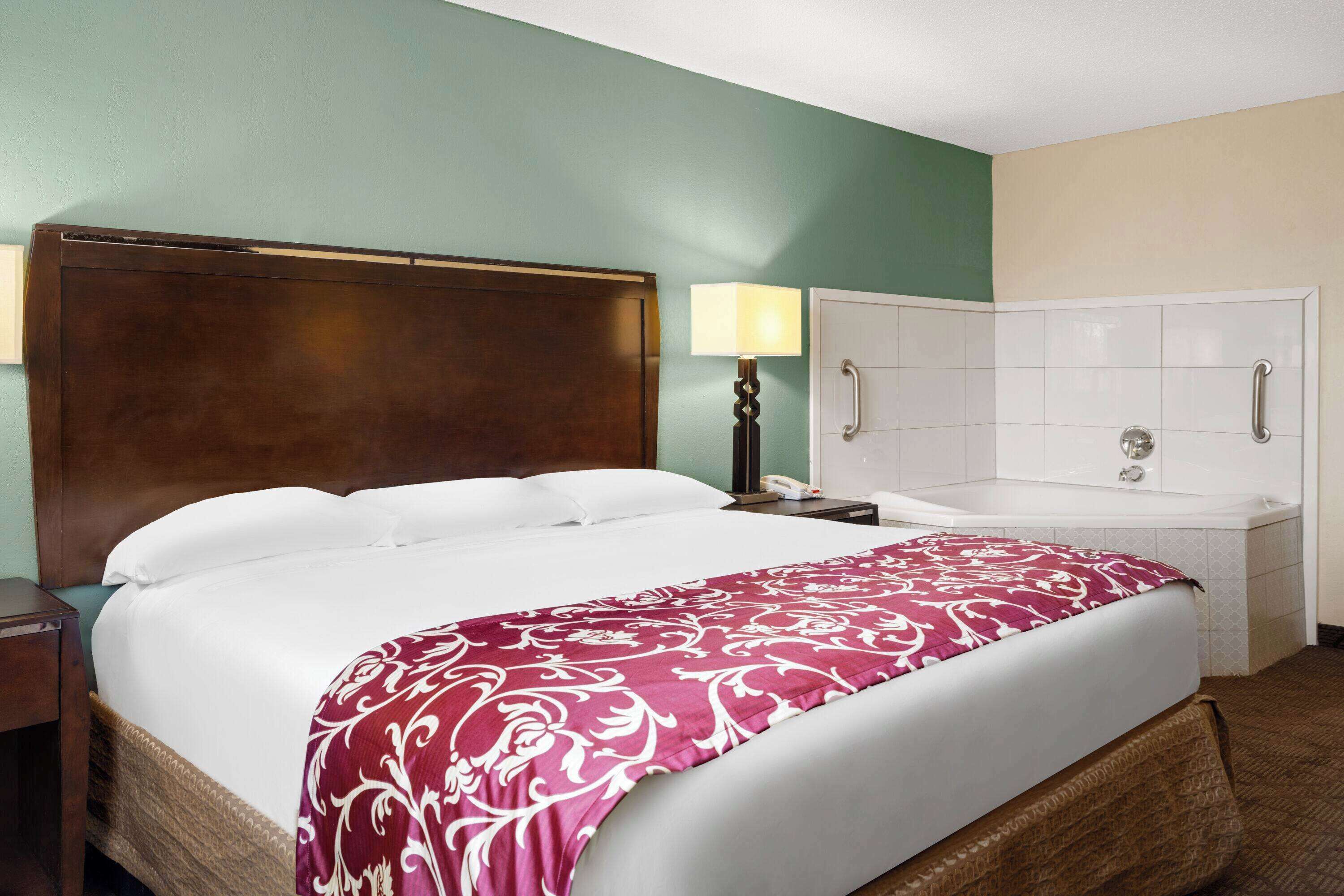 A hotel room with a large bed, a bedside lamp, a white bathtub, and a wooden headboard.