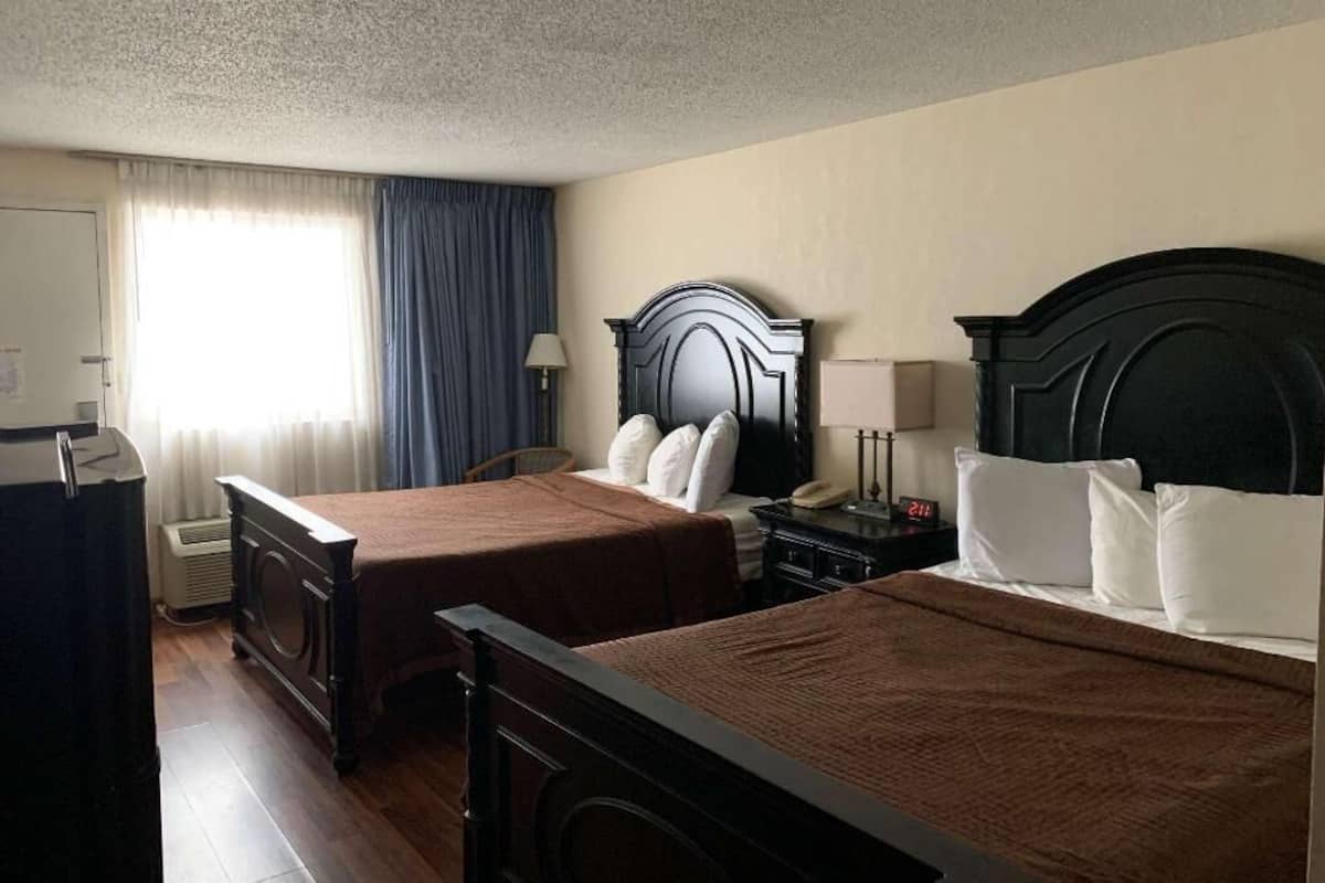 A hotel room with two beds, a desk, a lamp, a telephone, and a window with curtains.