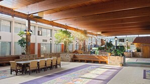 A spacious indoor area with a long table and chairs, benches, and potted plants.
