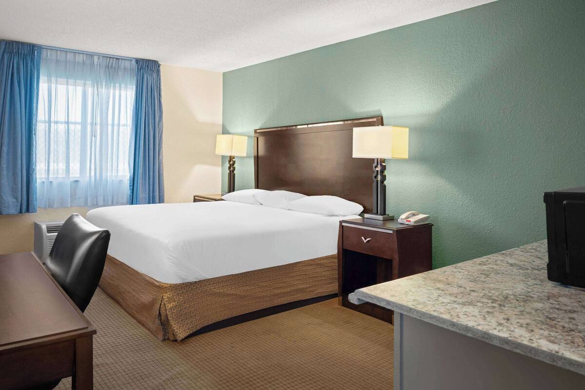 A hotel room with a large bed, two bedside tables with lamps, a desk, and a chair.