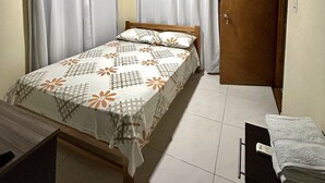 A bedroom with a bed, curtains, a wooden door, and a small table with a towel. - Apartamentos Katy (San Andrés)