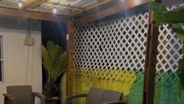 An outdoor patio area with wooden flooring, a covered seating area with chairs and a table, and a decorative lattice wall. - Apartamentos Katy (San Andrés)