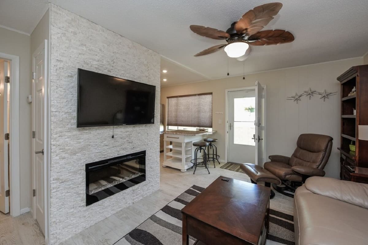 Una sala de estar con chimenea, ventilador de techo, televisor y un sillón de cuero.