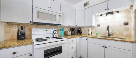 Cocina con armarios blancos, microondas, estufa y encimera de granito.
