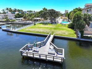 A dock with a bench and a small boat, a grassy area with a pool, and buildings in the background. - Sea Club II by Beachside Management (Siesta Key)