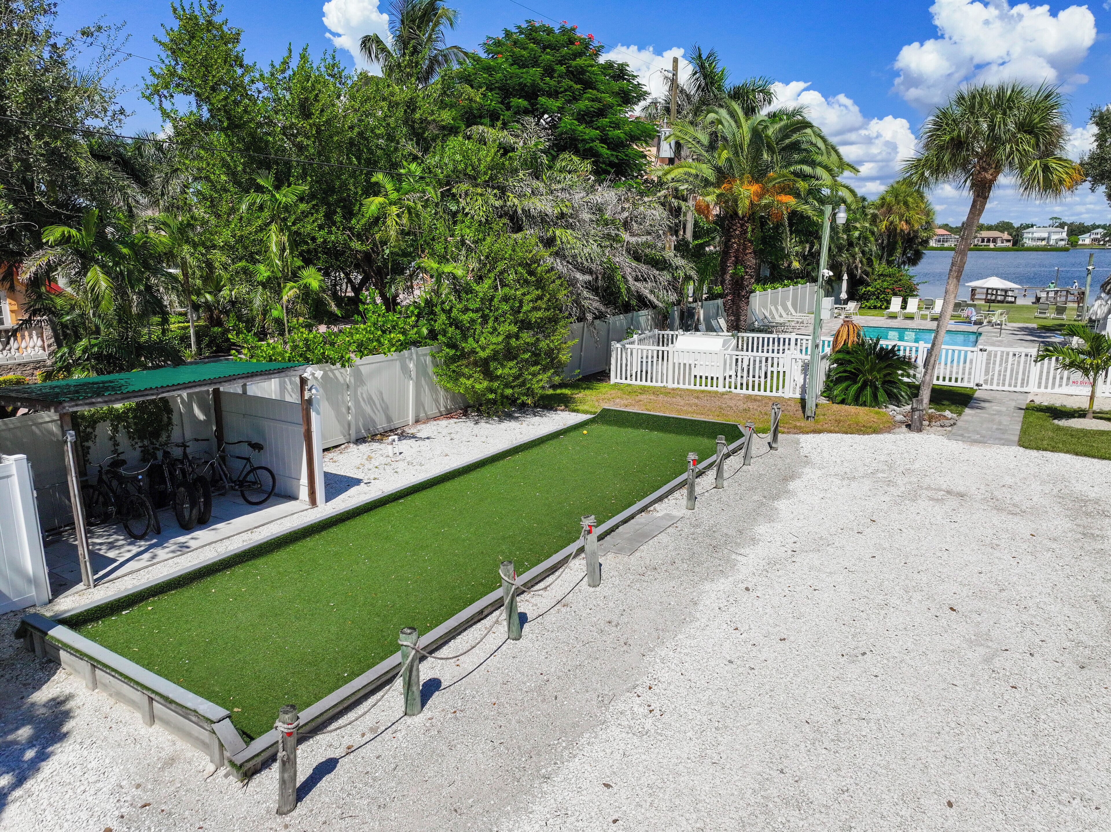 A pool area with a green artificial turf, white fence, and a covered seating area with chairs.