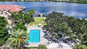 A swimming pool with a deck, surrounded by palm trees and a view of a lake. - Sea Club II by Beachside Management (Siesta Key)
