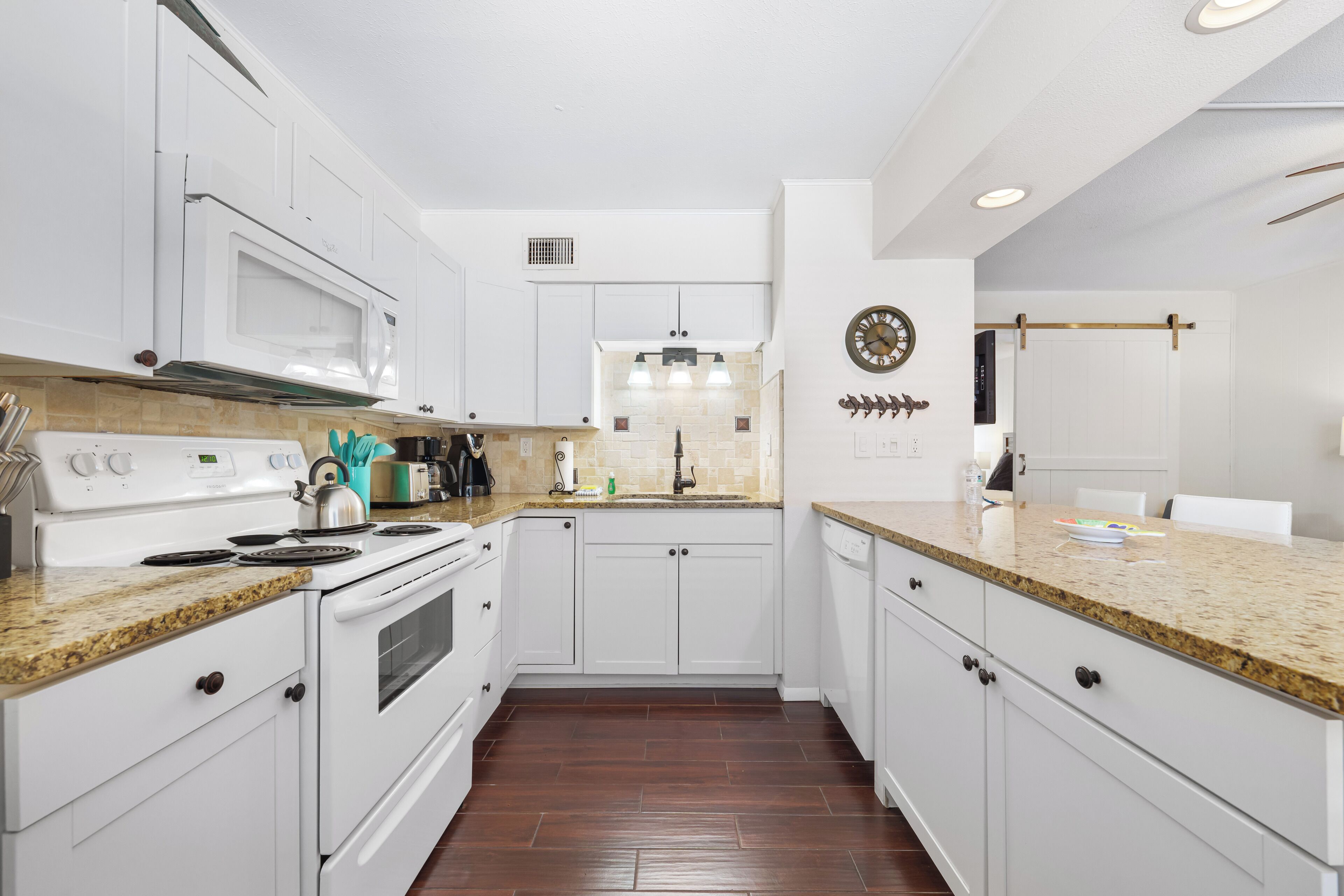 A modern kitchen with white cabinetry, a granite countertop, a built-in microwave, and a stainless steel range hood.