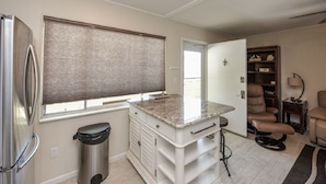 A compact kitchen with a built-in refrigerator, a window with blinds, a countertop, and a trash can. - Sea Club II by Beachside Management (Siesta Key)