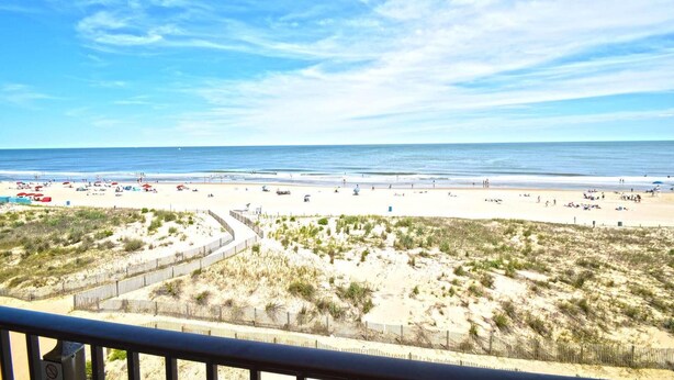 A beach with a wooden fence, sandy dunes, and the ocean in the background.