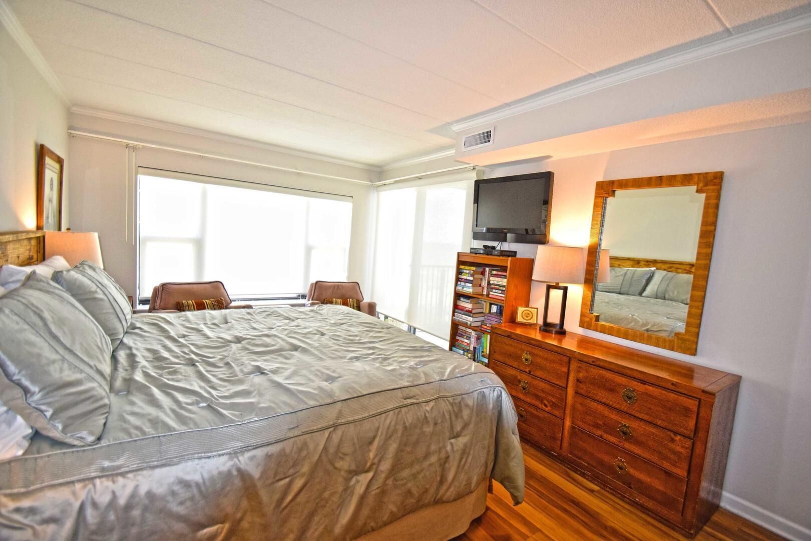 A bedroom with a large bed, a wooden dresser, a television, and a bookshelf.