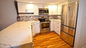 A modern kitchen with white cabinets, stainless steel appliances, a marble countertop, and wooden flooring.