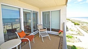 A balcony with a view of the beach, furnished with two chairs and a small table.