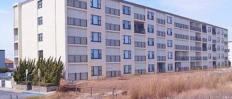 A multi-story residential building with a flat facade, balconies, and a parking area in front.