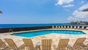 A pool with lounge chairs and a view of the ocean.