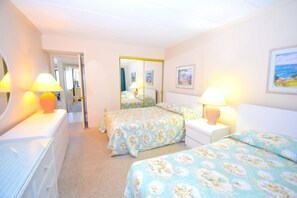 A hotel room with two beds, a large mirror, and a door leading to another room.