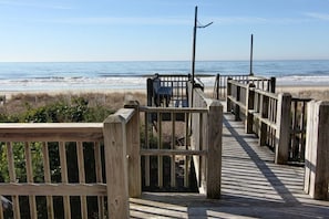 A wooden boardwalk leading to a beach with a bench and a flagpole.