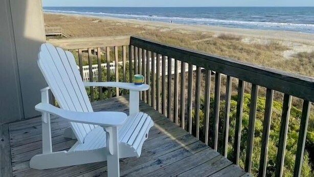 A wooden deck with a white Adirondack chair and a small table, overlooking a beach and ocean. - Eastside  3 Bedroom Home by RedAwning (Supply)