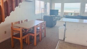 A living room with a wooden dining table, chairs, a sofa, a TV, and a kitchen area with cabinets. - Eastside  3 Bedroom Home by RedAwning (Supply)