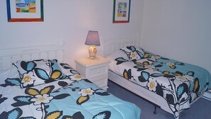 Une chambre avec deux lits simples, une table de chevet avec une lampe et deux tableaux encadrés au mur.