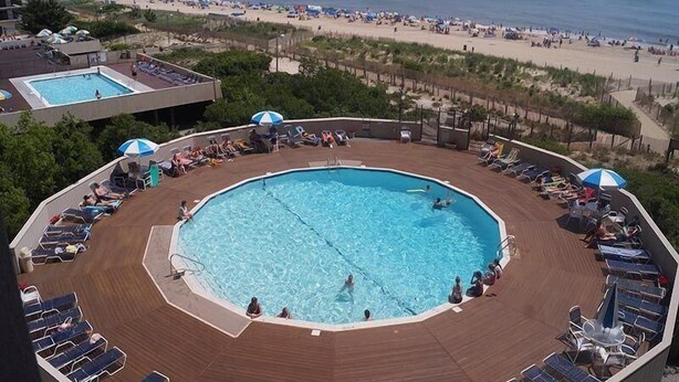 Un espace piscine doté d’une piscine circulaire, de chaises longues et de parasols.
