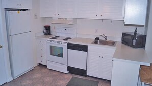 Une cuisine de taille réduite, avec des meubles blancs, une cuisinière, un lave-vaisselle, un four à micro-ondes et un réfrigérateur.