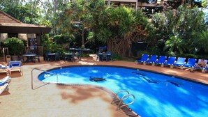 A swimming pool with lounge chairs and tables, surrounded by greenery. - Valley Isle 302 by RedAwning (Lahaina)