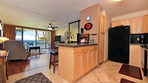 A modern kitchen with wooden cabinets, a black refrigerator, and a dining area with a view of the ocean. - Valley Isle 302 by RedAwning (Lahaina)