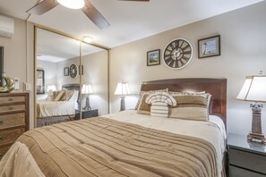 A bedroom with a large bed, a mirror, a clock, and a nightstand with a lamp.
