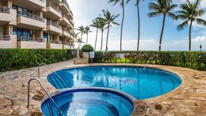 A swimming pool with a stone deck, surrounded by palm trees and a multi-story building with balconies. - Paki Maui #109 1 Bedroom Condo by RedAwning (Lahaina)