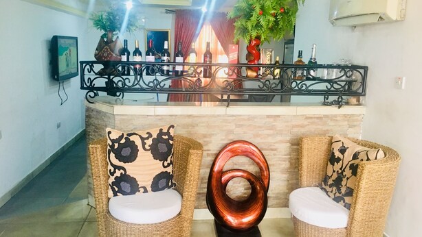 Un hall con sillas de mimbre, una baranda metálica decorativa y una exhibición de botellas de vino.