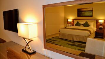 A hotel room with a bed, bedside lamps, a flat-screen TV, and a mirror reflecting the room.