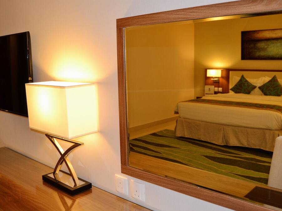 A hotel room with a bed, bedside lamps, a flat-screen TV, and a mirror reflecting the room.