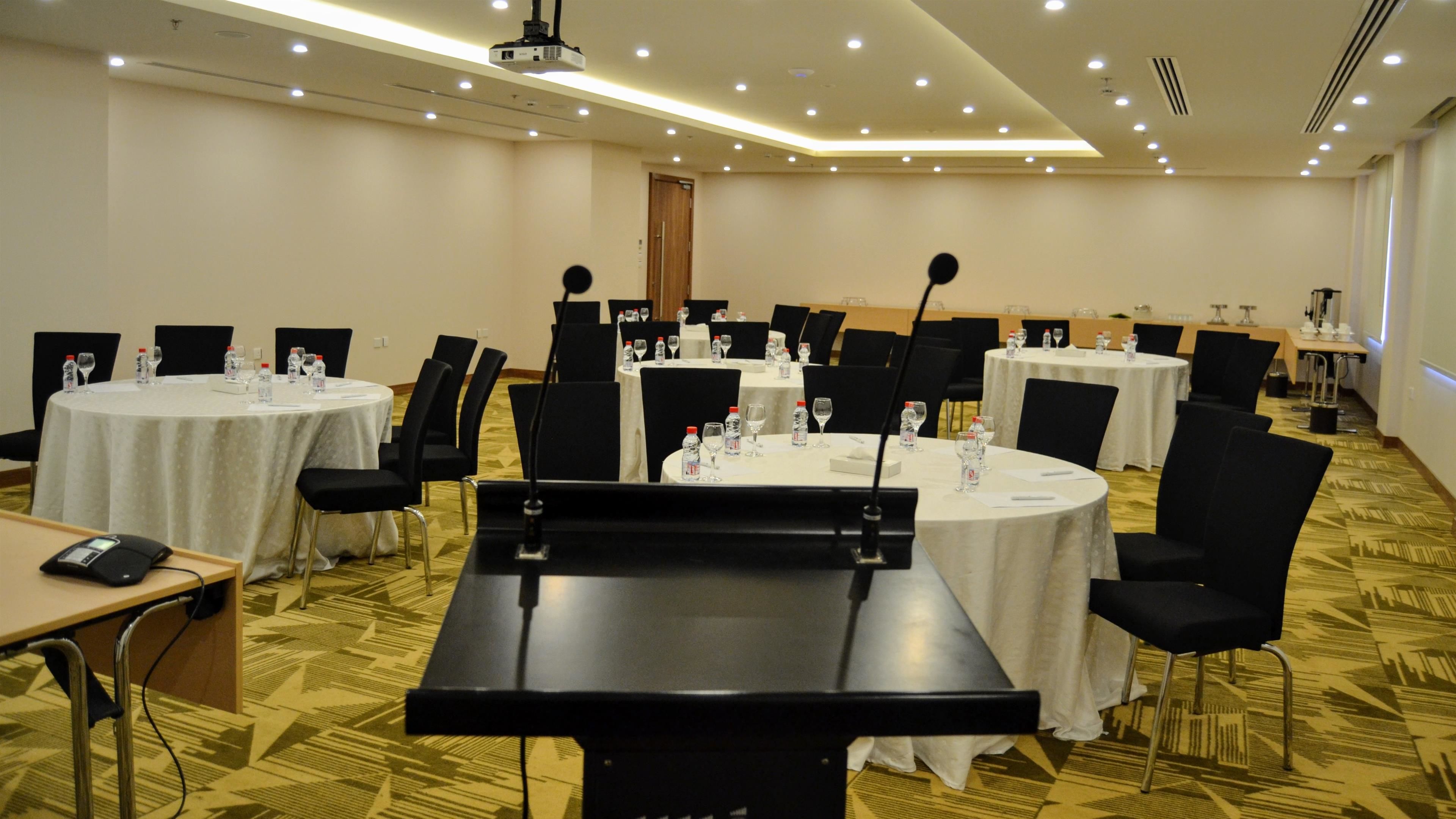 Une salle de conférence avec des tables rondes, des chaises noires et un pupitre.
