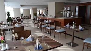 En restaurant i et hotel med flere borde, stole og en buffet.