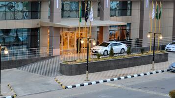 A modern building with a glass facade, a covered entrance, and a parking area with a white car.