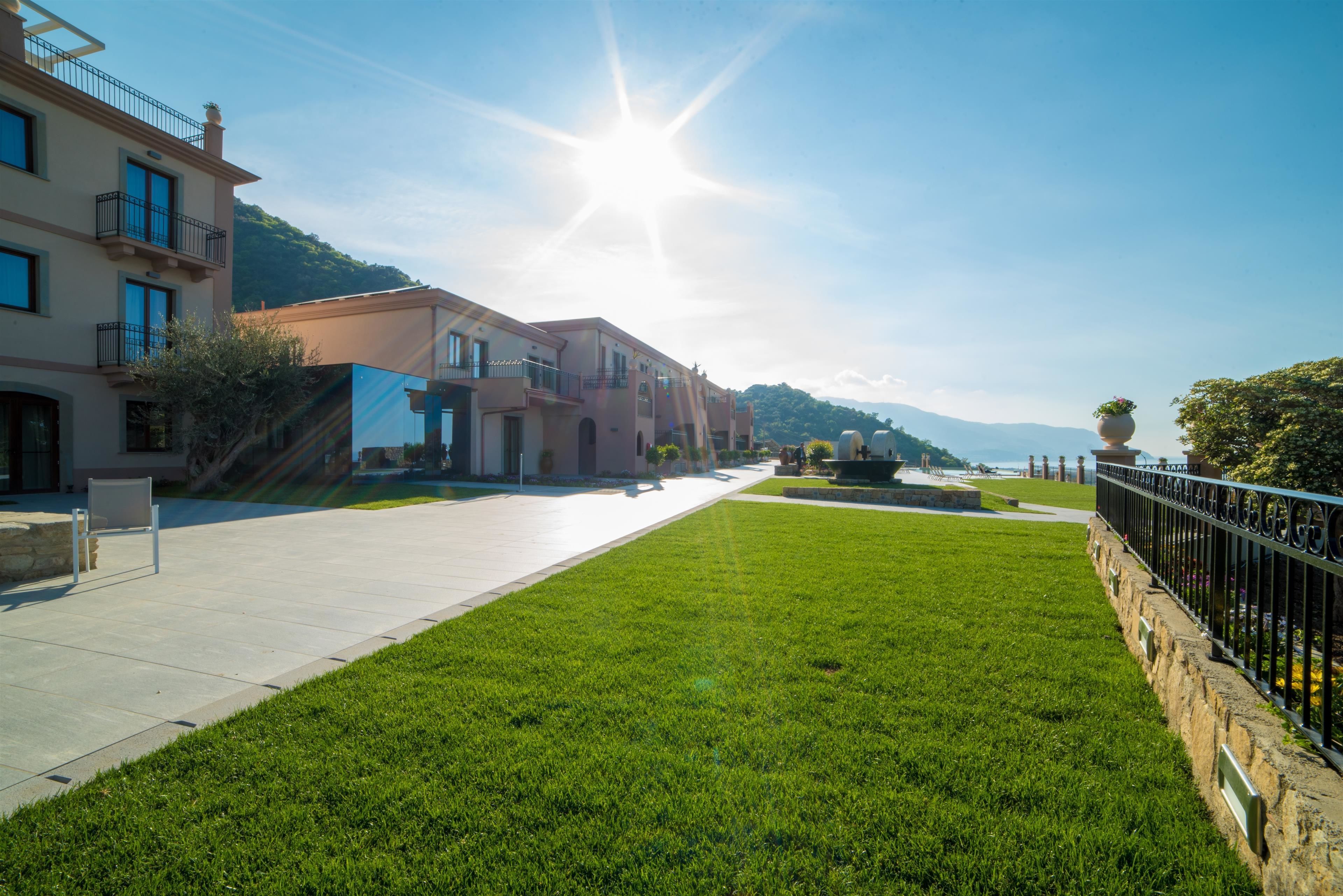 A sunny street with a grassy median, buildings with balconies, and a clear sky.