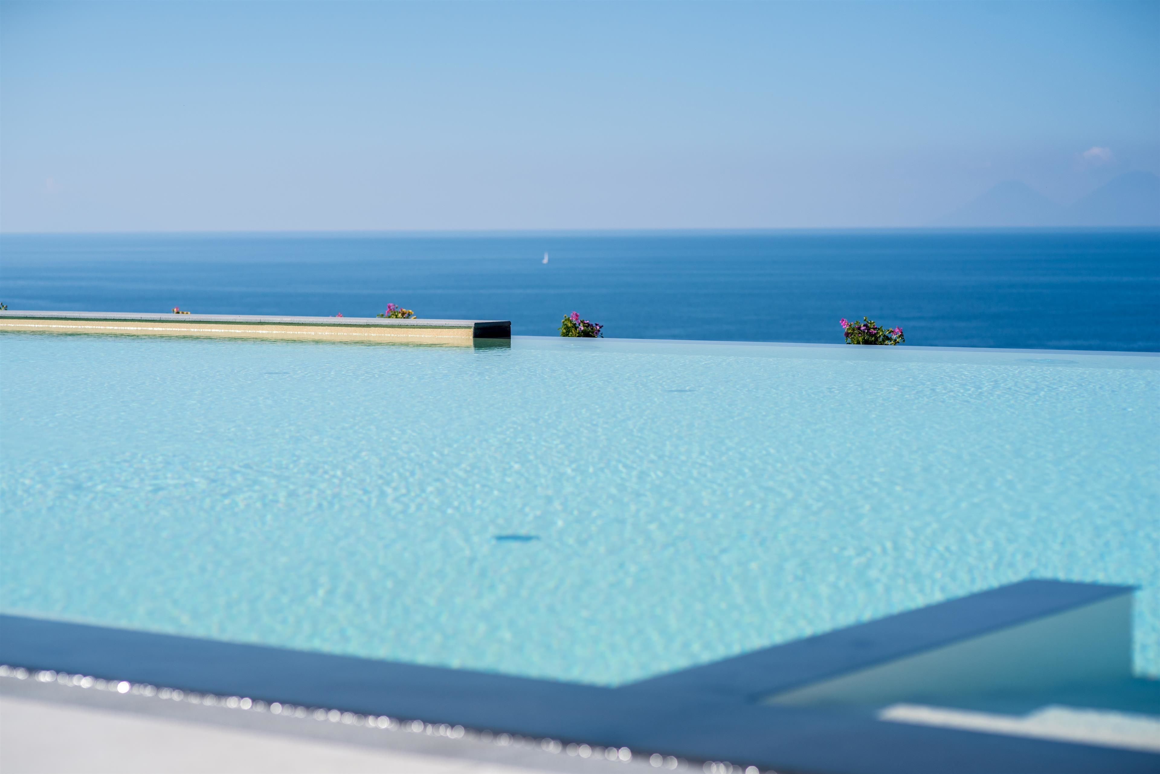 A pool with a clear view of the ocean and a distant sailboat.