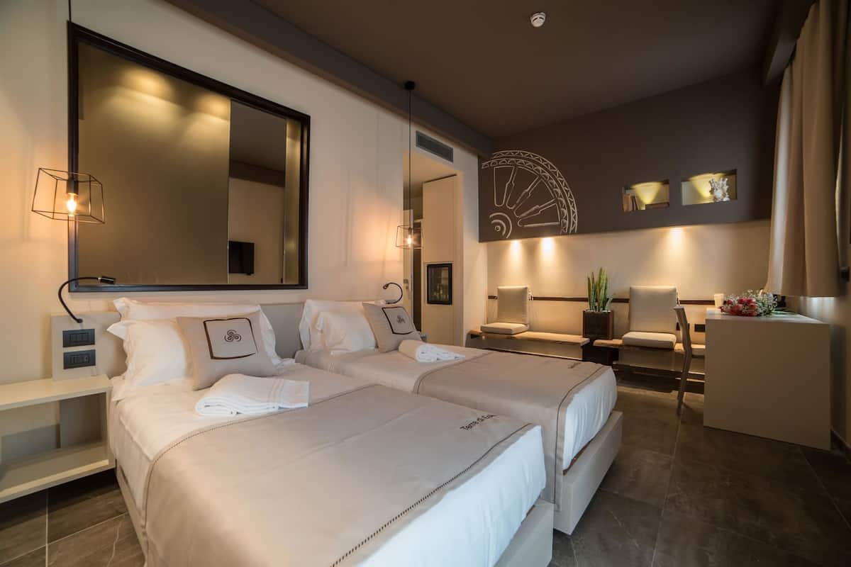 A hotel room with two beds, a desk, a chair, a large mirror, and a decorative wall piece.