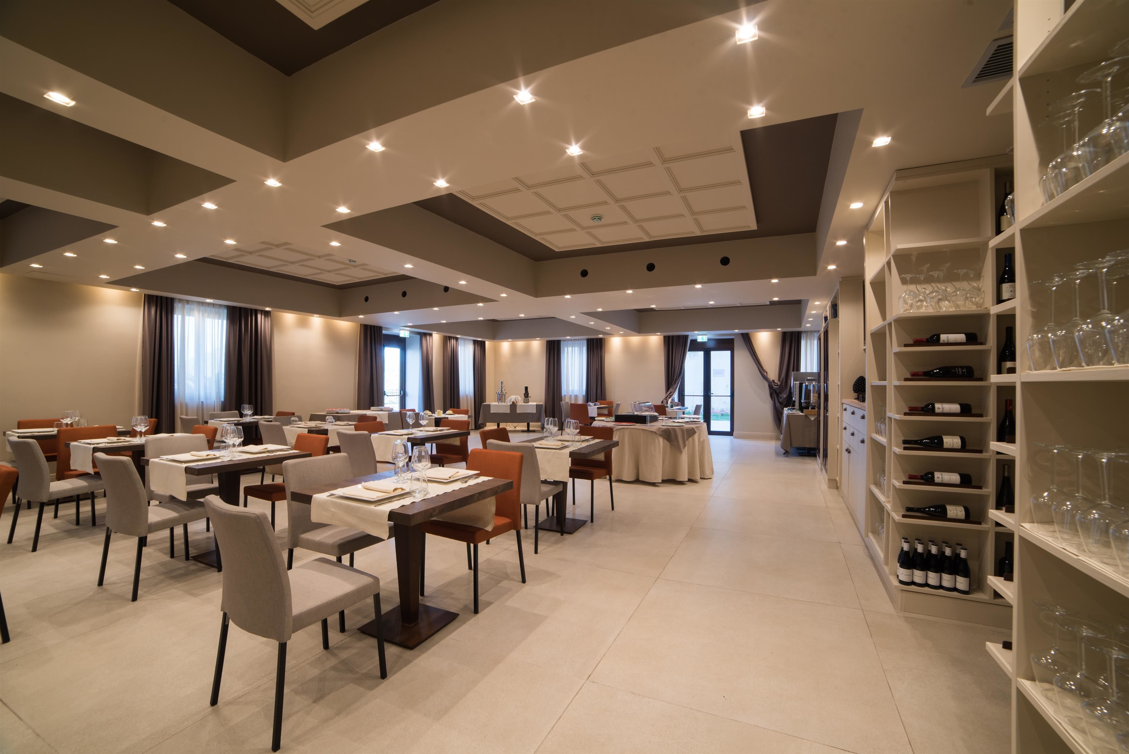 A spacious dining area with multiple tables and chairs, a wine rack with bottles, and a view of the city through large windows.