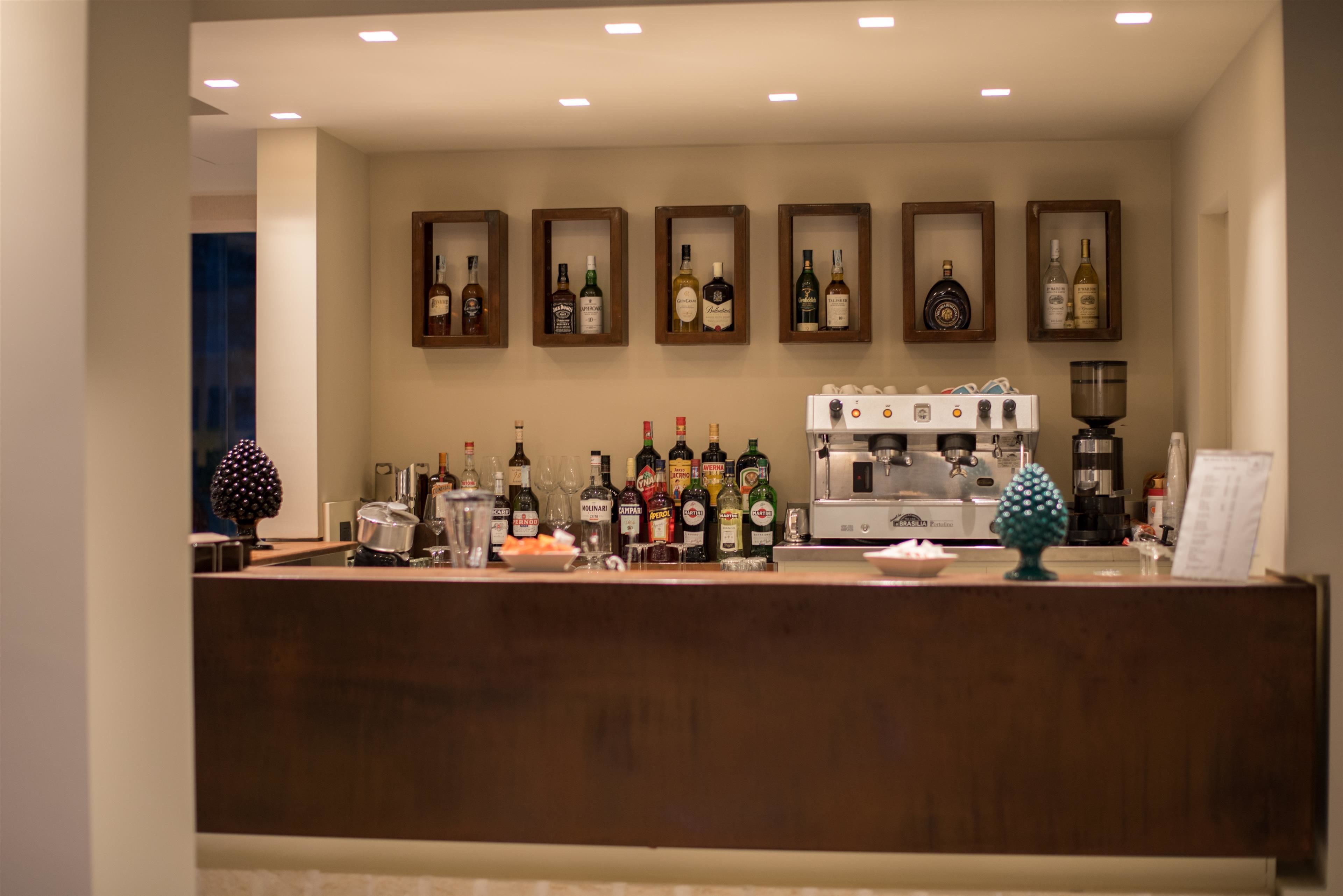 Una zona de bar con mostrador de madera, varias botellas de licor, vasos y una máquina de café.