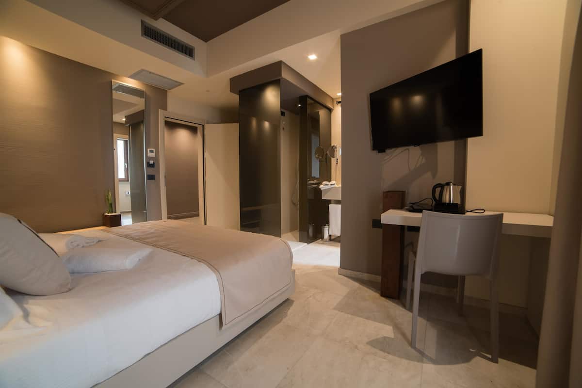 A modern hotel room with a large bed, a desk, and a flat-screen TV mounted on the wall.