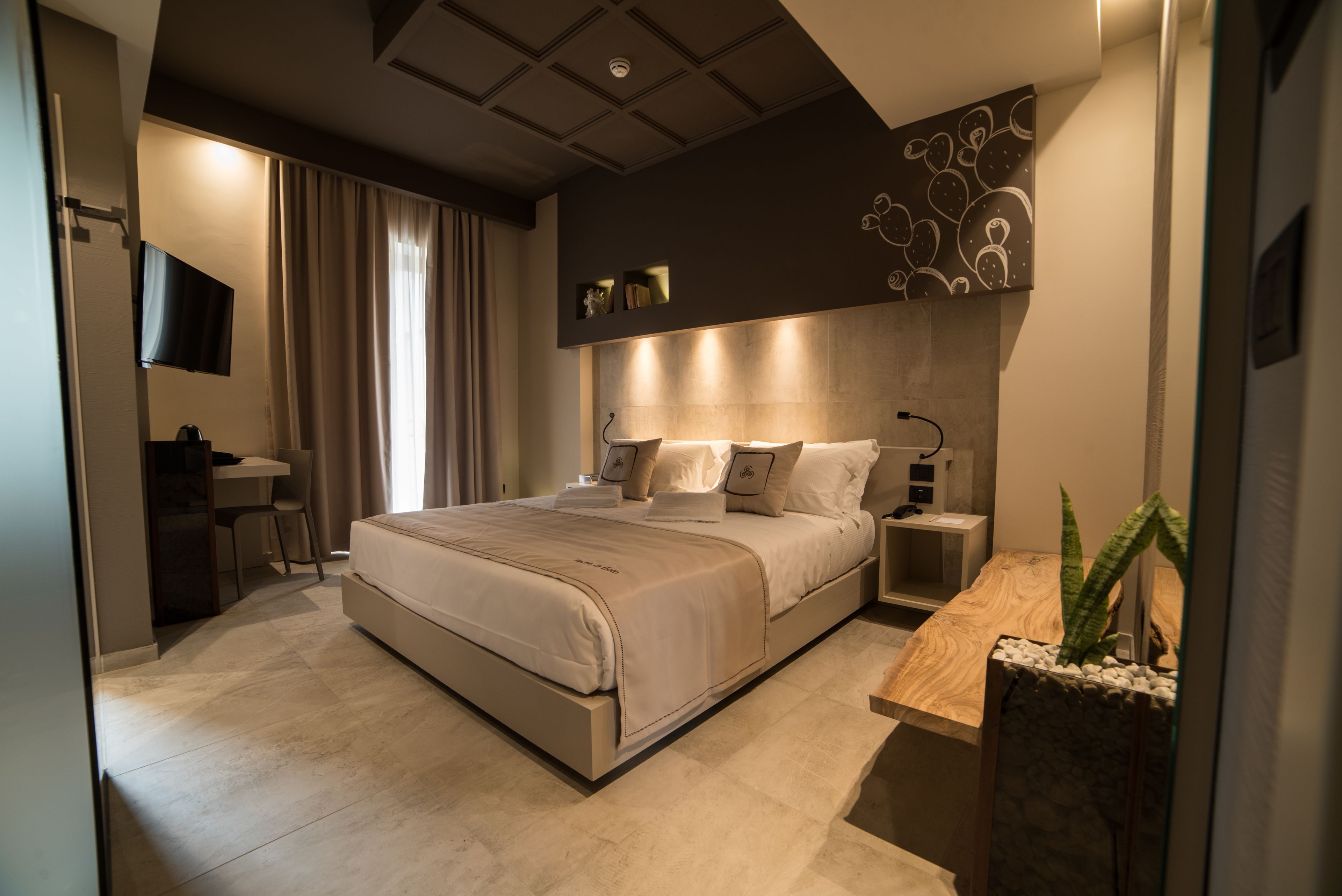 A modern bedroom with a large bed, bedside tables, a desk, and a TV.