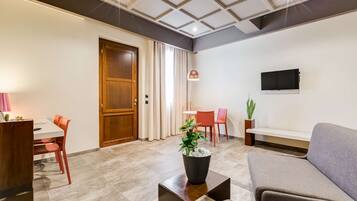 Ein modernes Wohnzimmer mit einer Couch, einem Esstisch mit Stühlen, einem an der Wand befestigten Fernseher und einem Blumentopf auf einem Couchtisch.